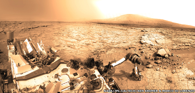 a mosaic shot from Curiosity's Mastcam showing the rover at "Yellowknife Bay" with the robot arm deployed during drill tests and "Mount Sharp" on the horizon. The rover's mast cannot be seen as it is compltely outside the Mastcam's field of view and so cannot be imaged