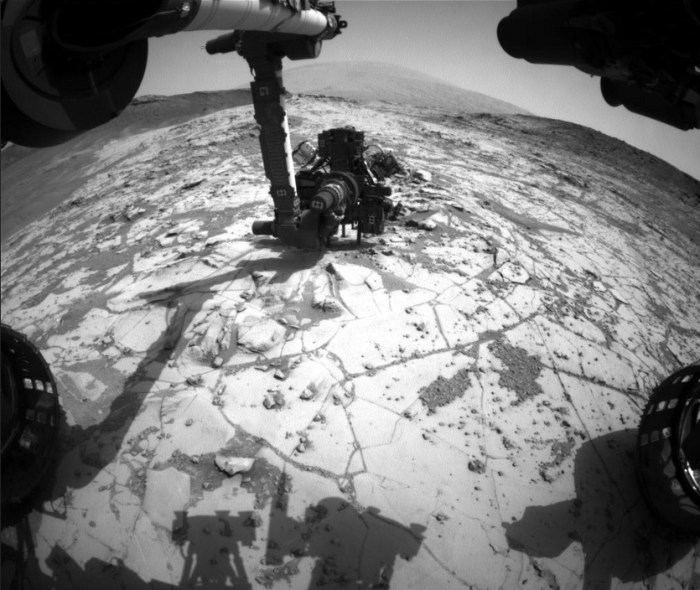 A unique view of the "mini drilling" operation on "Mojave". Captured by Curiosity's Hazcam navigation cameras, the image shows the rover's "hand" oriented such that the dril (visible with its two steadying arms) is placed against the rock