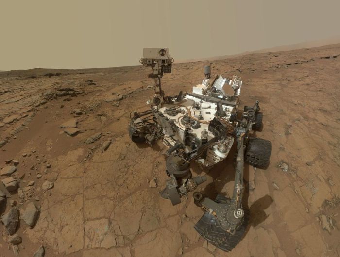 An updated version of Curiosty's "selfie" from February 2013, when the rover was examining the rock dubbed "John Klein".  The original image rendered a "fishbowl" look; in this revised image, the background has been flatened and rendered as seen from a single point in the camera's field of view, while the view of Curiosity is made up of a number of images captured by the rover's Mars Hand Lens Imager (MAHLI)