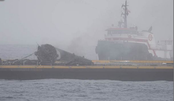 With the towing vessel for the autonomous droneship approaching in the background, a photo from one of the landing support vessels shows the Falcon 9 1st stage toppled over on the landing ship's deck after one of its legs broke on touchdown